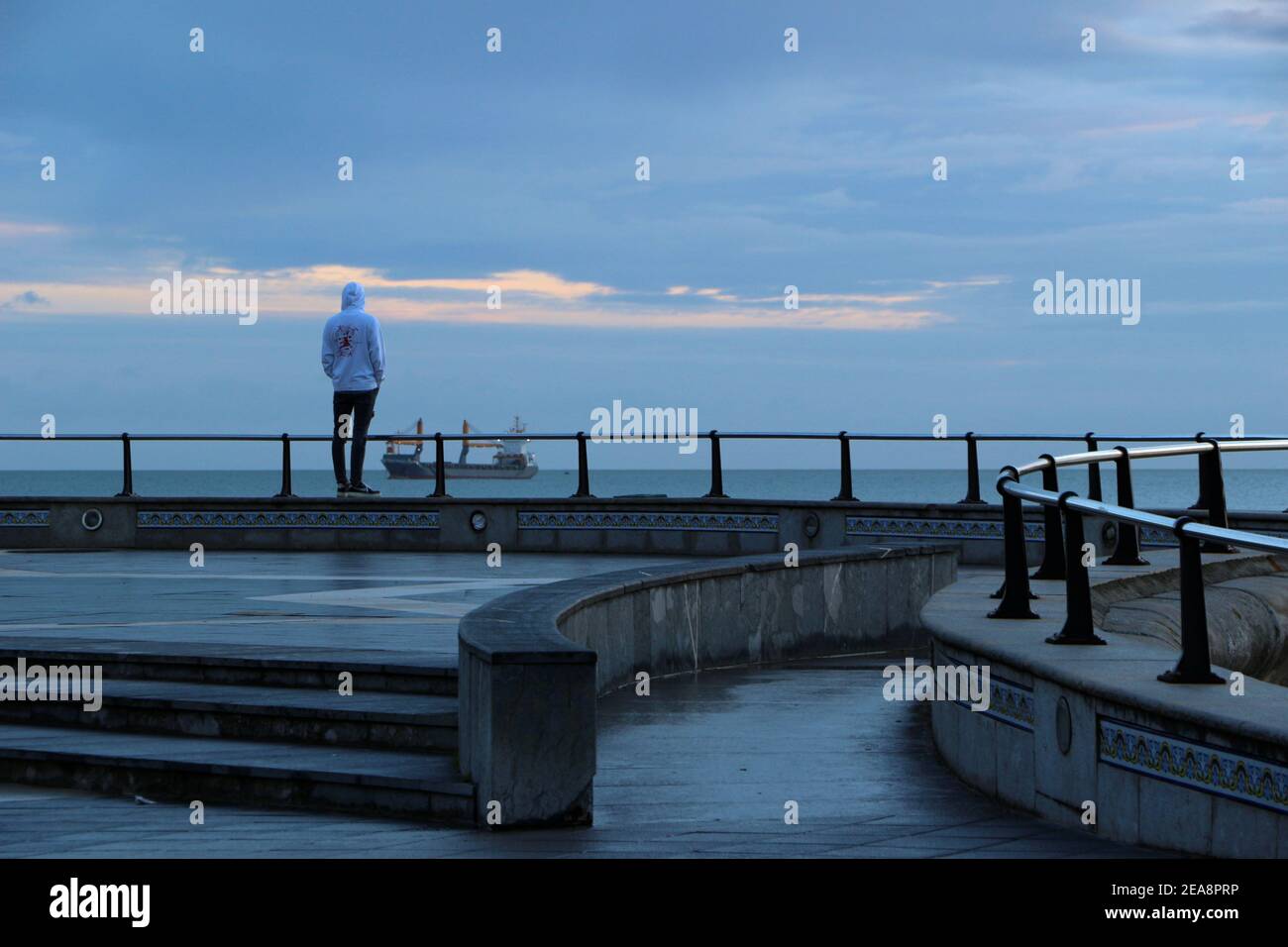 Giovane uomo che indossa una felpa con cappuccio che guarda verso il mare in una nave ancorata al largo della costa di Santander Cantabria Spagna Inverno Foto Stock