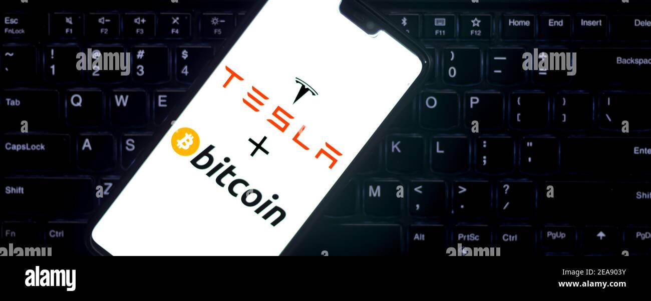 Logo Bitcoin su uno smartphone contro il logo Tesla sullo sfondo. Foto Stock