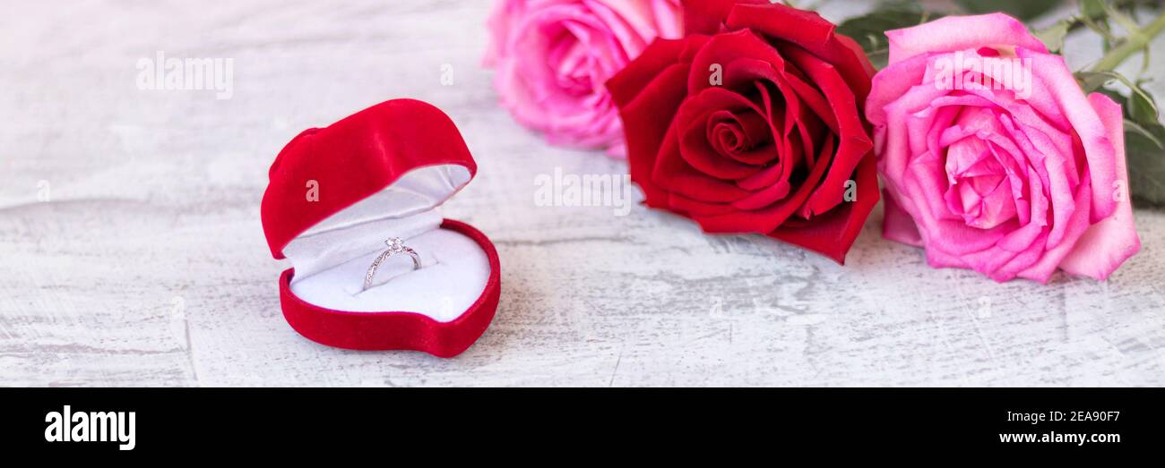 Striscione con anello di nozze all'interno della scatola di velluto rosso  per l'anello di aggancio accanto al bouquet di rose. Regalo romantico per  San Valentino. Proposta di matrimonio conc Foto stock 