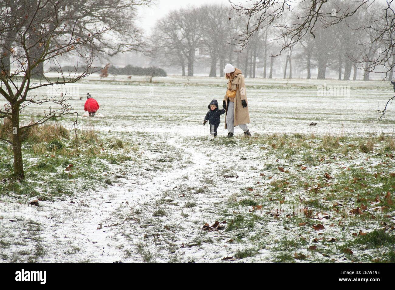 Una donna e un bambino camminano attraverso un bordo innevato del Wastead Park nella parte est di Londra. La neve e il ghiaccio pesanti hanno portato disagi in alcune parti del Regno Unito, con Londra che riceve circa 5 cm di neve. I forti venti orientali di Storm Darcy hanno precipitato le temperature in alcune parti del Regno Unito a meno di uno. Foto Stock