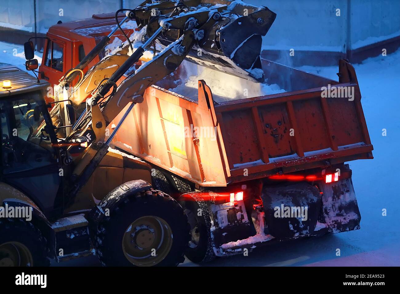 Un escavatore carica la neve nella parte posteriore di un dumper di notte. Foto Stock
