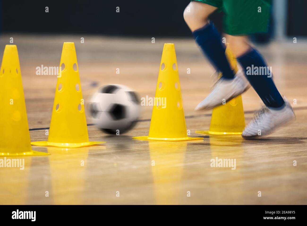 Giocatore che pratica il calcio indoor Dribbling abilità che corre tra i coni di addestramento gialli. Unità di formazione Futsal per la squadra giovanile Foto Stock