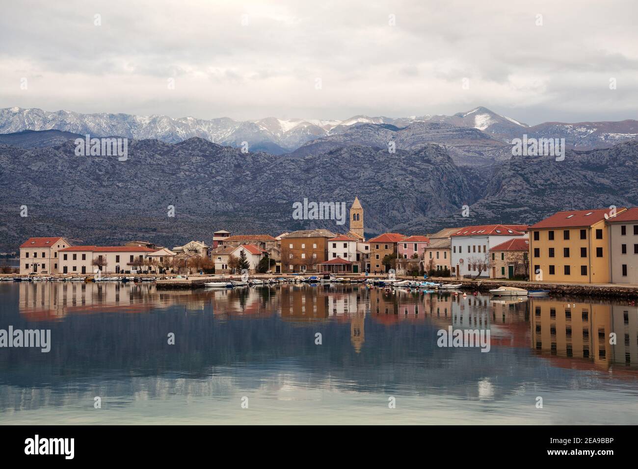 Piccola città costiera di Vinjerac in Croazia al mattino presto con mare calmo, riflessi in acqua e montagne sullo sfondo. Foto Stock