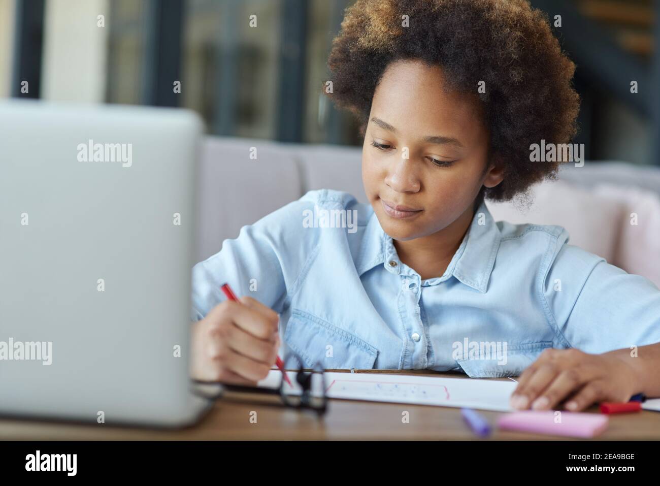 Più tempo per l'arte. Razza mista scolara disegno su carta con marcatori colorati mentre studiando con laptop a casa durante la quarantena Foto Stock