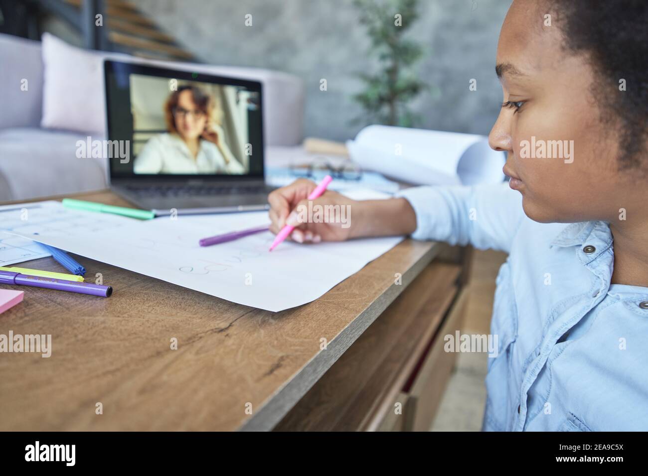 Primo piano di disegno studentessa teen con marcatori durante online lezione con l'insegnante tramite l'app di videochat mentre studia da casa Foto Stock