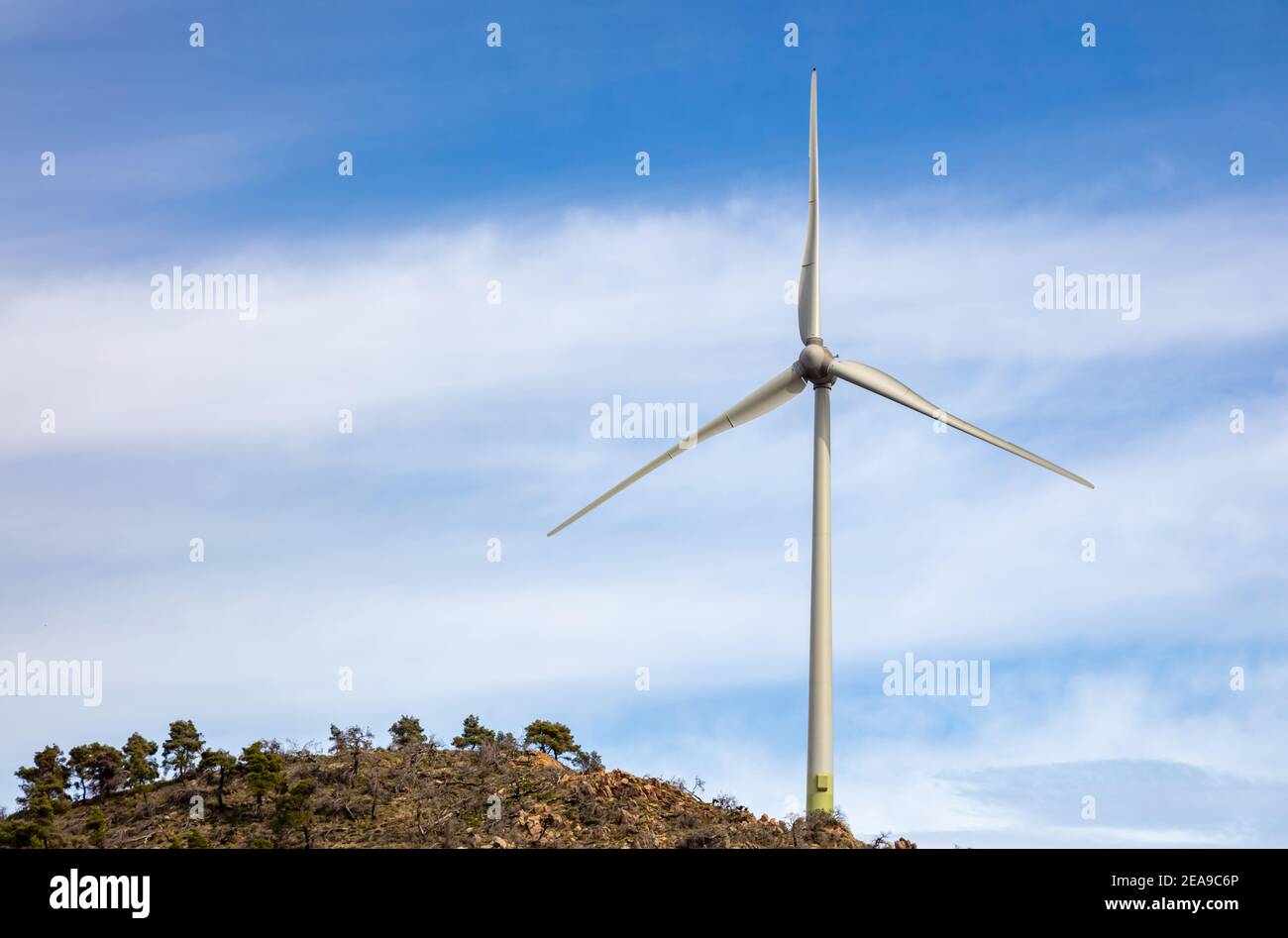 Turbina eolica sulla cima della collina rocciosa, vista aerea del drone, generazione di energia alternativa, cielo blu nuvoloso, verde eco-industria rinnovabile Foto Stock