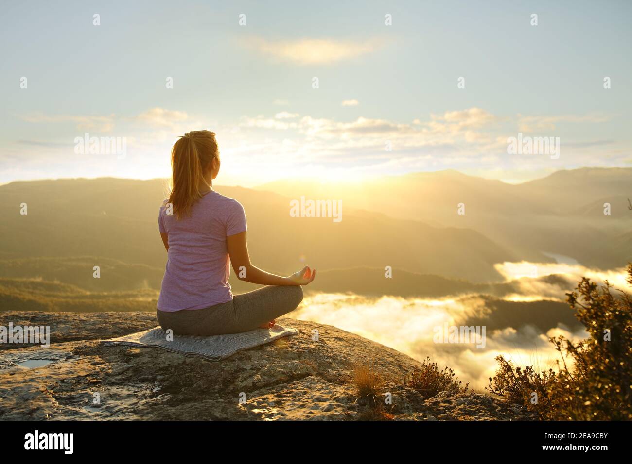 Donna che medita praticando l'esercizio di yoga in montagna al tramonto Foto Stock