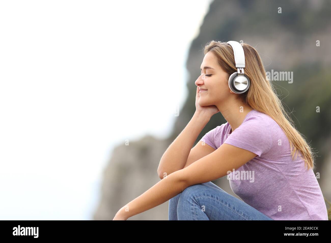 Profilo di una donna rilassata che ascolta la musica indossando il wireless cuffie in montagna Foto Stock