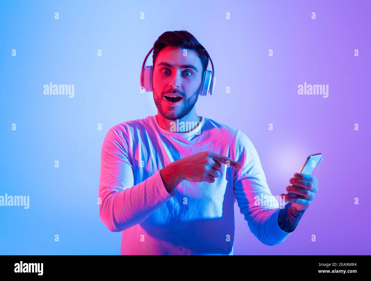 Un ragazzo millenario emozionato con un look a bocca aperta in cuffia alla telecamera Foto Stock