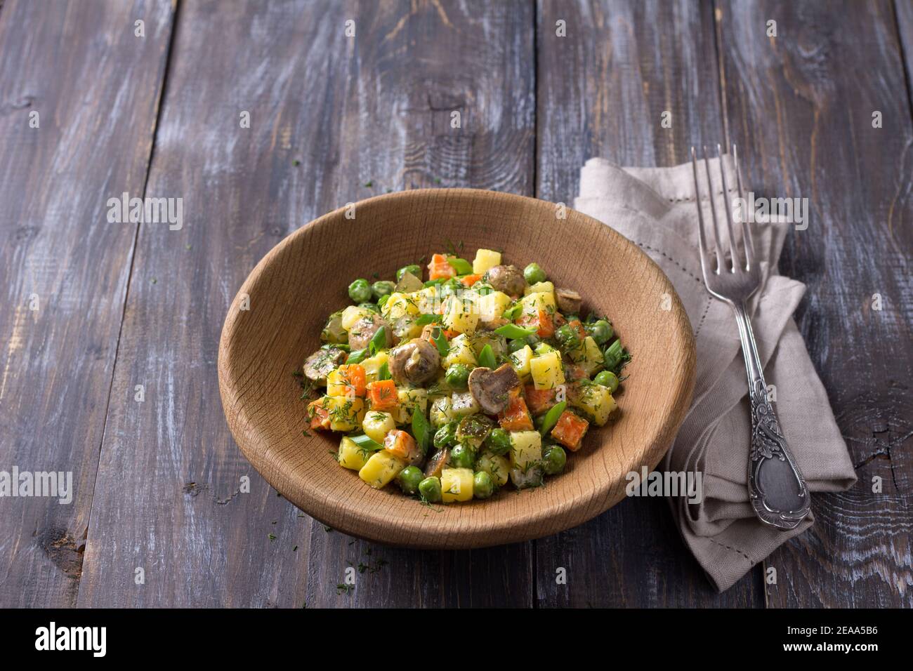 Insalata vegetariana invernale con funghi, insalata russa, maionese fatte in casa in una ciotola di legno su un tavolo di legno, stile rustico, orizzontale Foto Stock