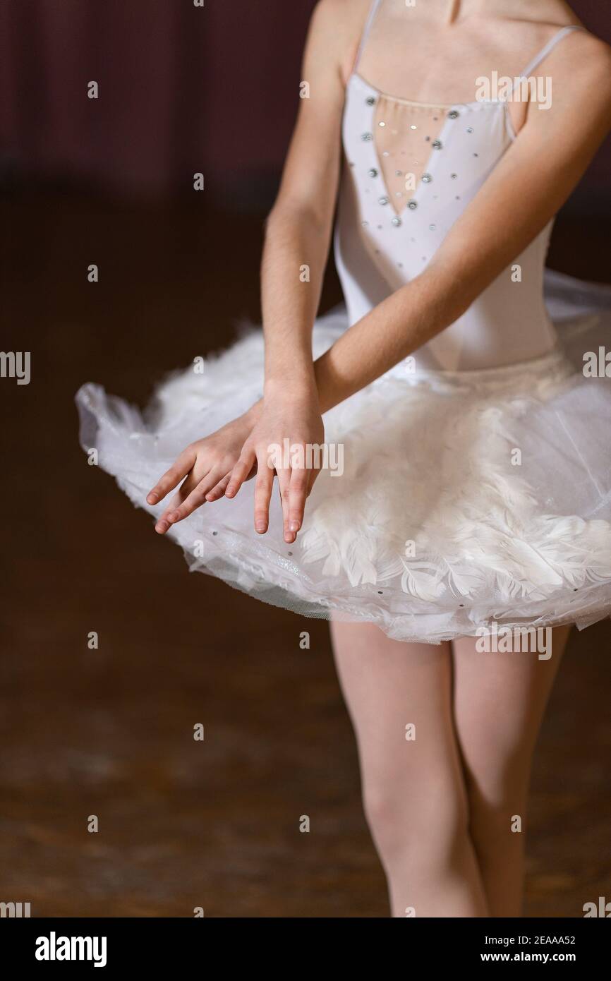 Ballerina giovane con mani e gambe incrociate e gonna bianca sul palco. Concetto di performance del balletto Foto Stock