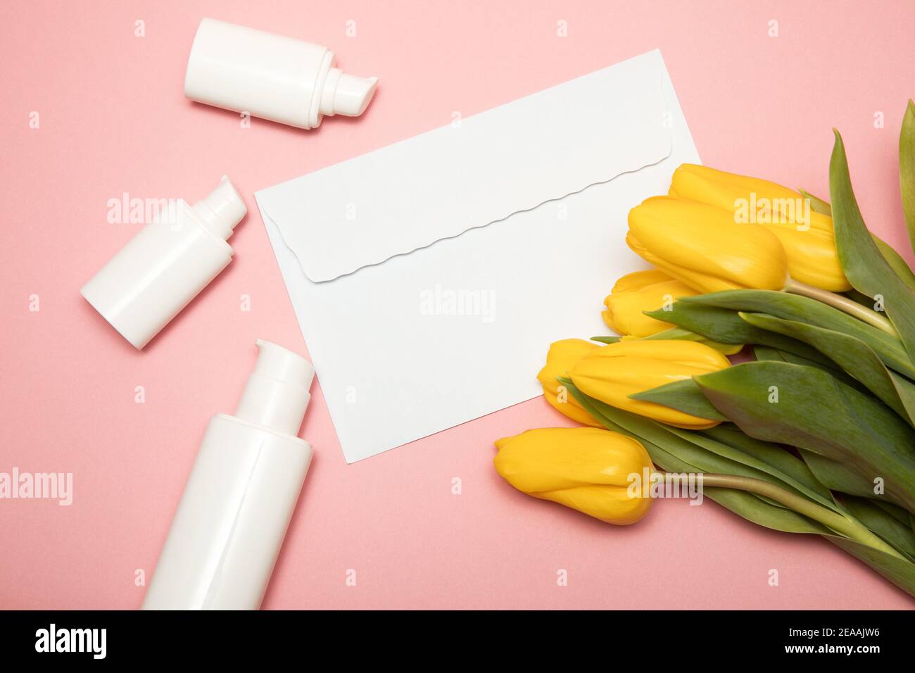 Tulipani gialli su sfondo rosa con busta copyspace e contenitori per bottiglie cosmetiche. Bock up. Buon giorno della madre, congratulazioni per la giornata delle donne Foto Stock