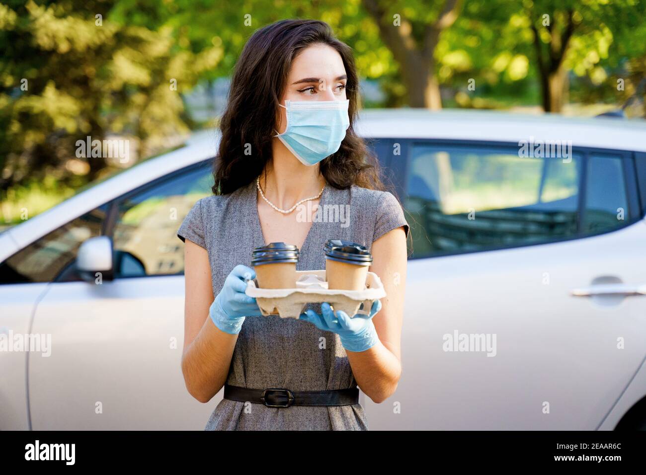 Consegna in auto del caffè dalla caffetteria. Cocee in tazza di cartone eco-usa e getta. Giovane ragazza lavora in agenzia di consegna e consegna caffè in auto. 4 co Foto Stock