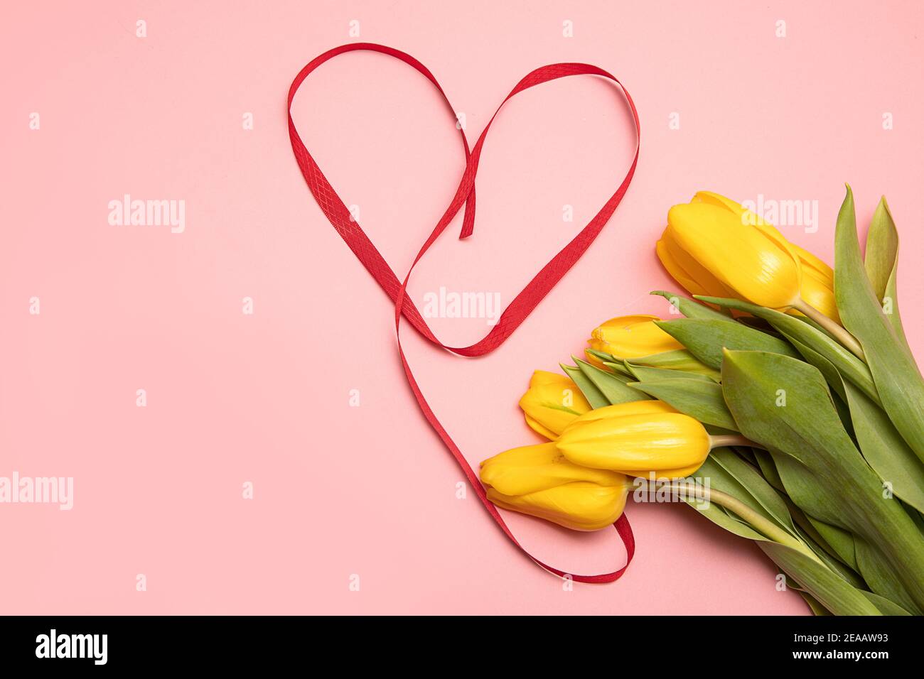 Bouquet di tulipani gialli e cuore fatto di nastri rossi su sfondo rosa con spazio copia. Concetto regalo per il giorno della mamma o di San Valentino Foto Stock
