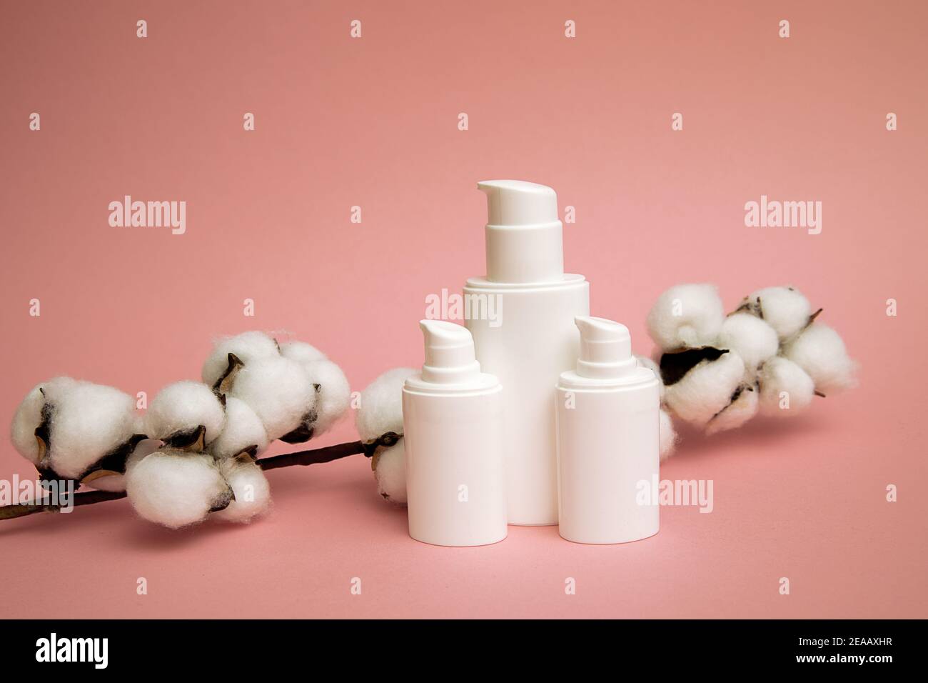 Contenitore bianco per bottiglia cosmetica in plastica con fiore di cotone, etichetta vuota per il marchio mock-up, concetto di prodotto Natural Beauty. Sfondo rosa Foto Stock