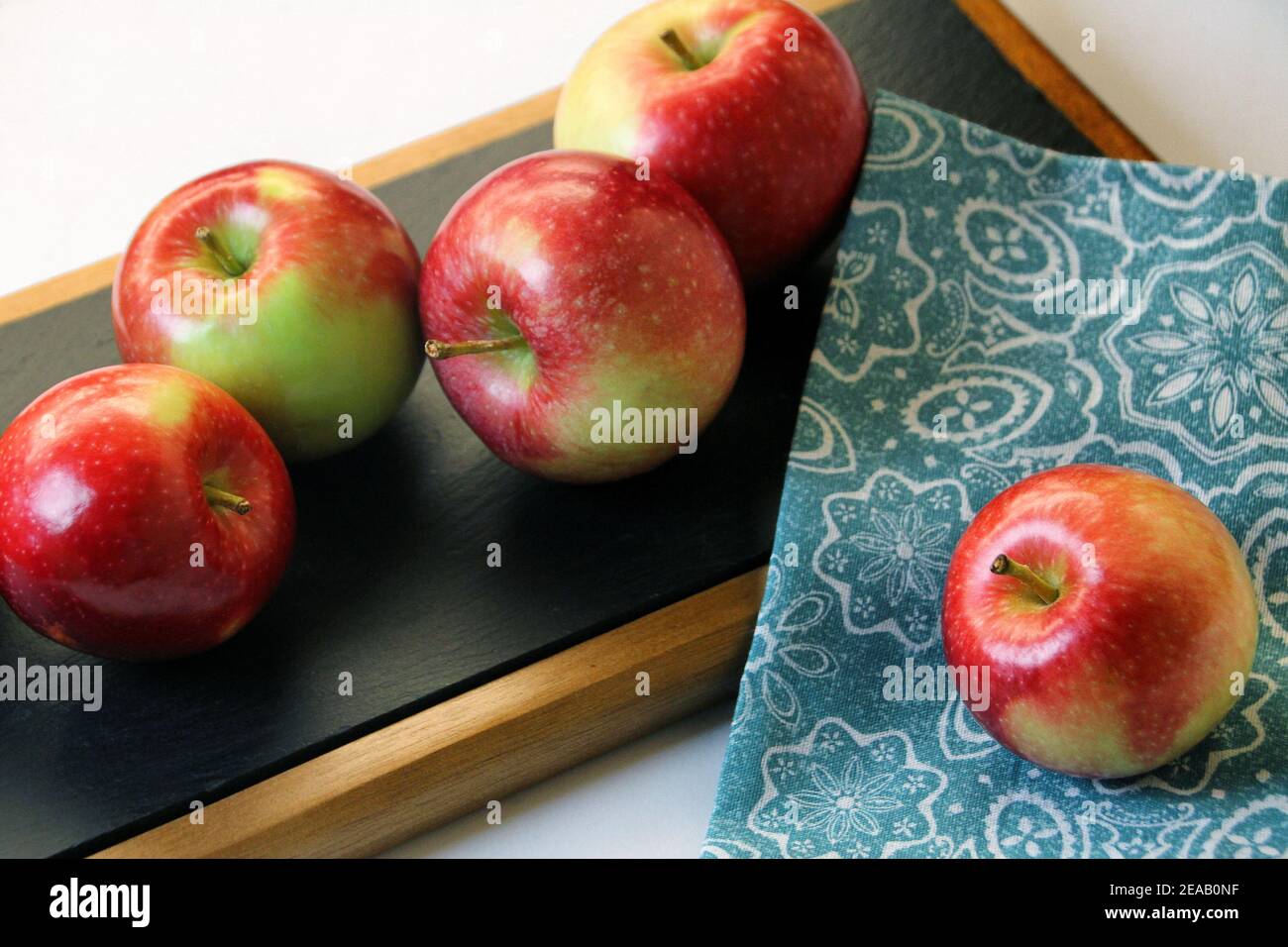 Quattro mele rosse Fuji sono raggruppate su un vassoio di portata nero con un'altra posta su una servietta blu. Foto Stock