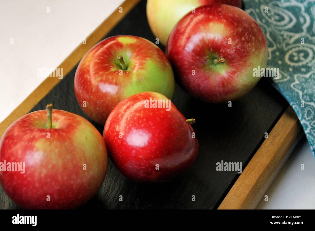 Cinque mele Fuji rosse sono raggruppate come una vita still usando una tavola di servizio del formaggio e una serviette blu e bianca. Foto Stock