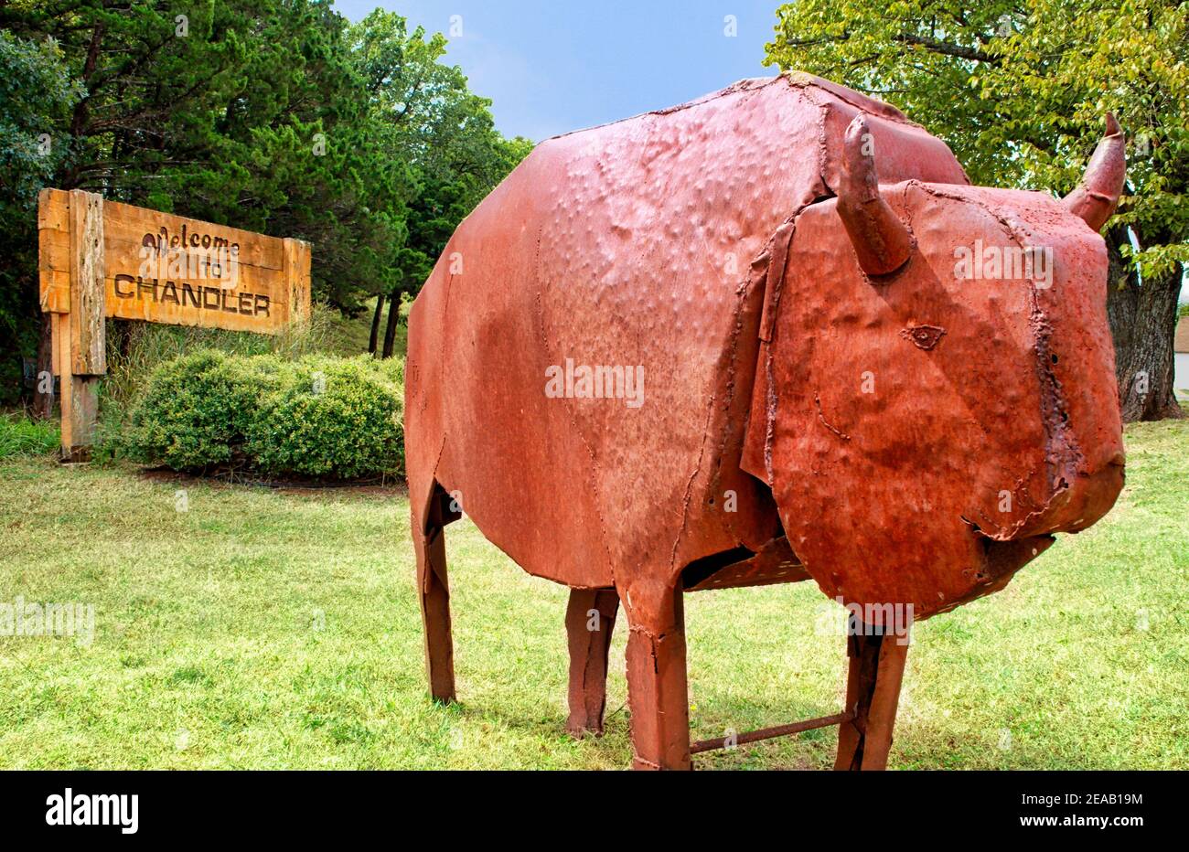 Una scultura rustica in metallo di un bisonte si trova di fronte a un cartello di benvenuto a Chandler, Oklahoma, lungo la Route 66. Foto Stock