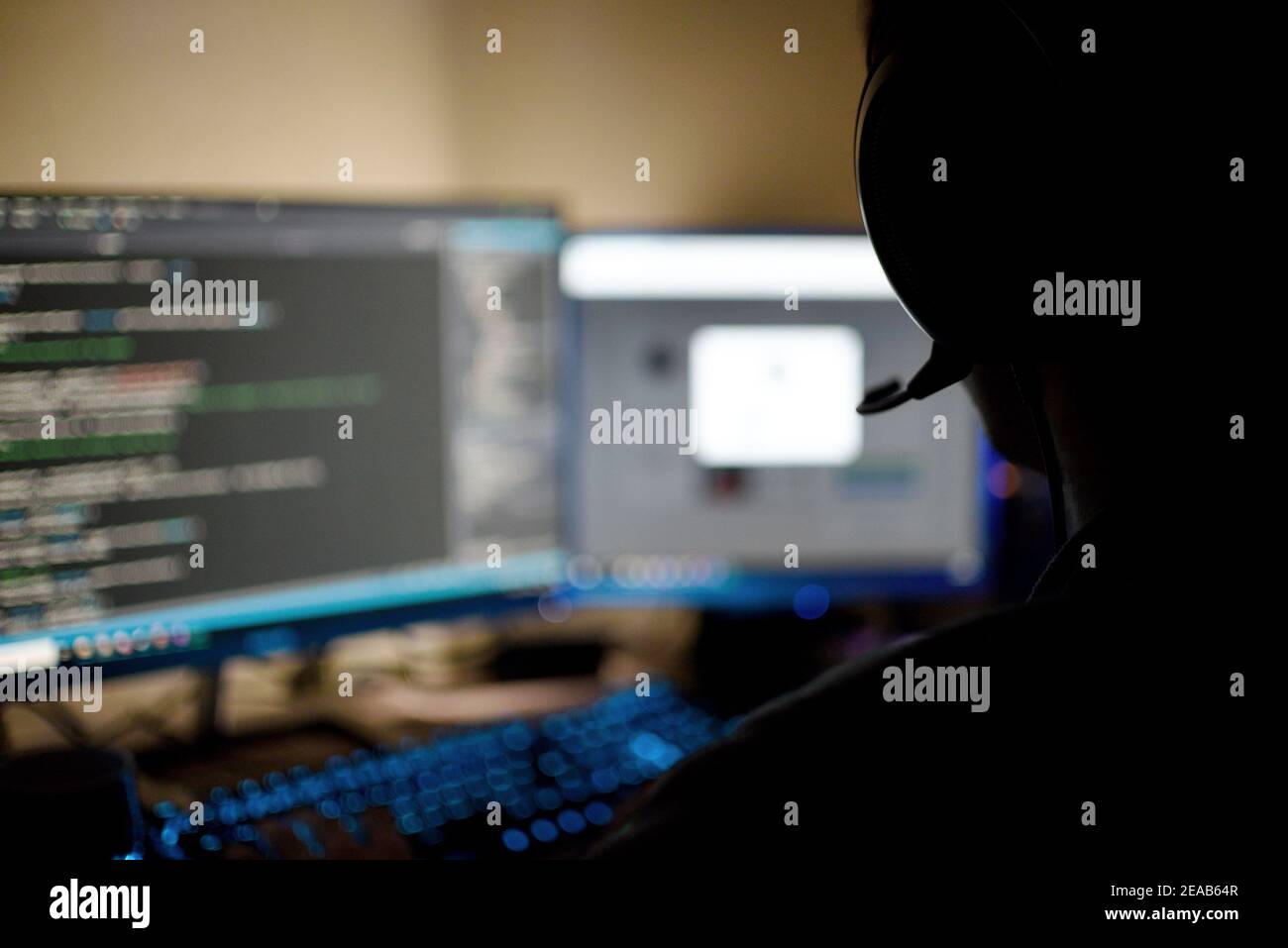 persona con le cuffie che utilizza due monitor per computer a casa Foto Stock