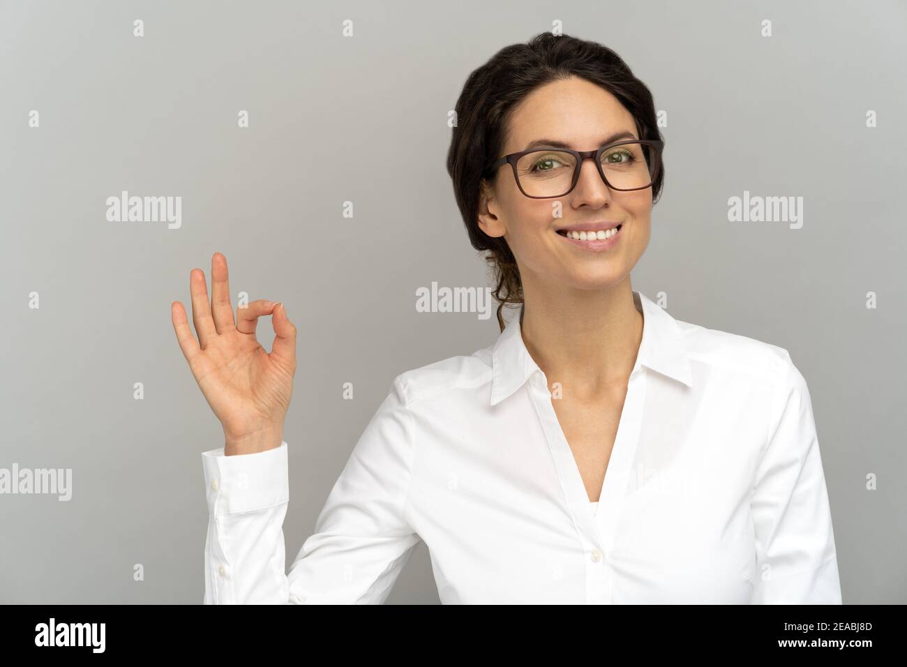 Allegra donna d'affari indossare una blusa di buon umore sorridendo ampiamente, mostrando un gesto OK in studio. Foto Stock