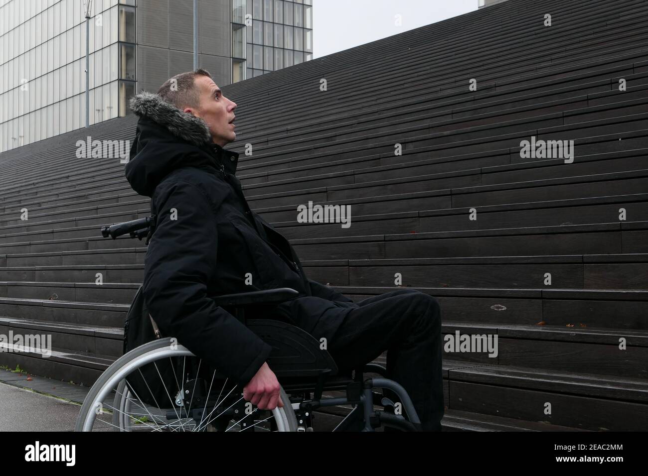 Concetto di persona disabile. Uomo in sedia a rotelle all'esterno della strada di fronte alle scale. Foto Stock