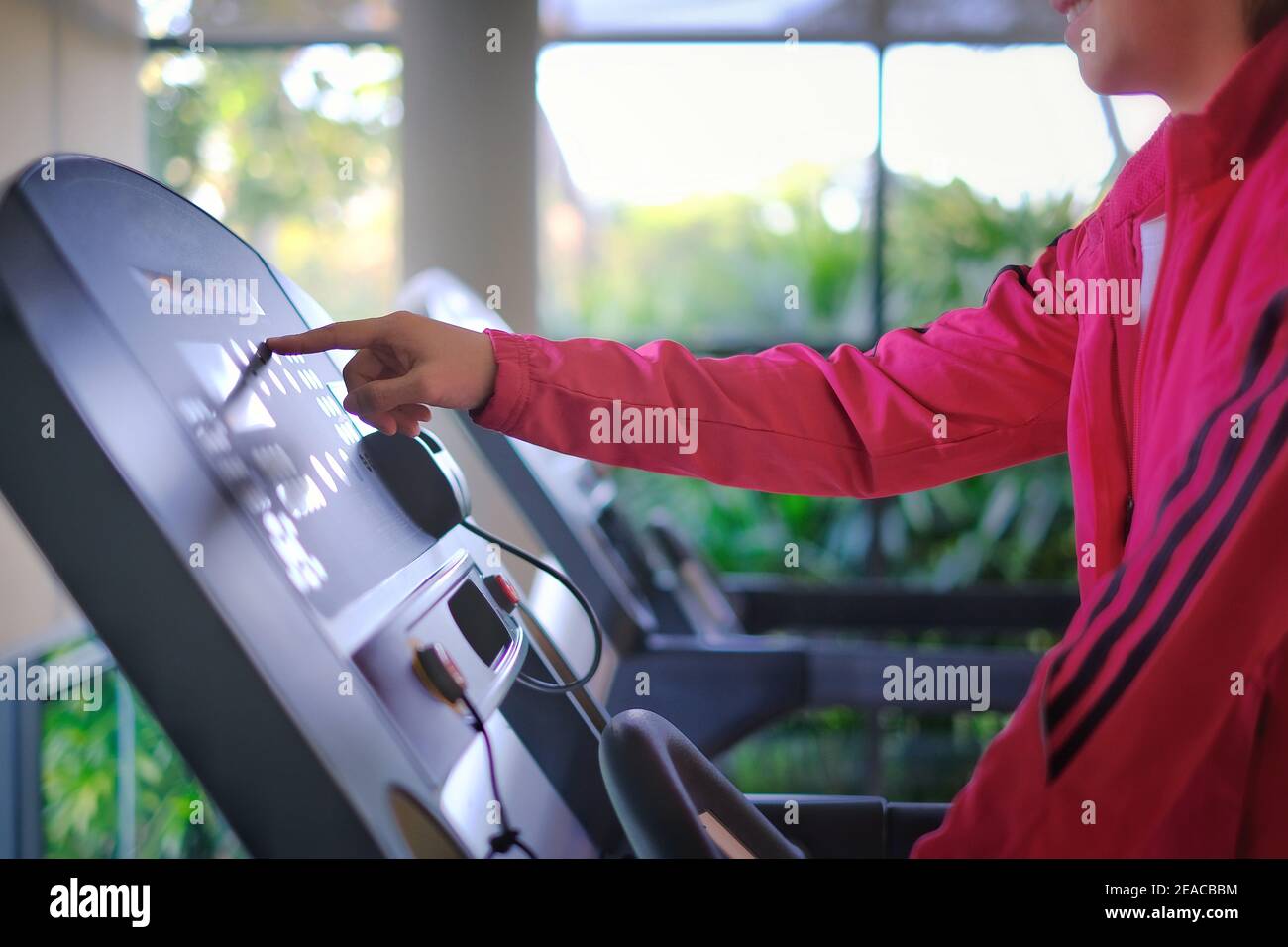 Una donna che si allenava in palestra su un tapis roulant, raggiungendo il monitor touch screen per modificare l'impostazione della velocità. Foto Stock Una donna che si allenava in palestra su un tapis roulant, raggiungendo il monitor touch screen per modificare l'impostazione della velocità. Foto Stock