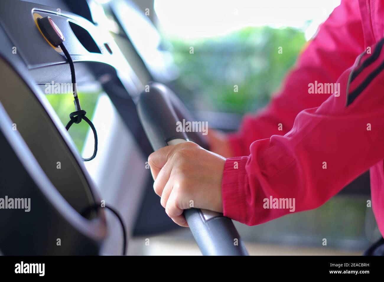 Una giovane donna asiatica in giacca sportiva rosa brillante si sta allenando in palestra, correndo su un tapis roulant, sentendosi stanca ma felice, sorridente. Foto Stock