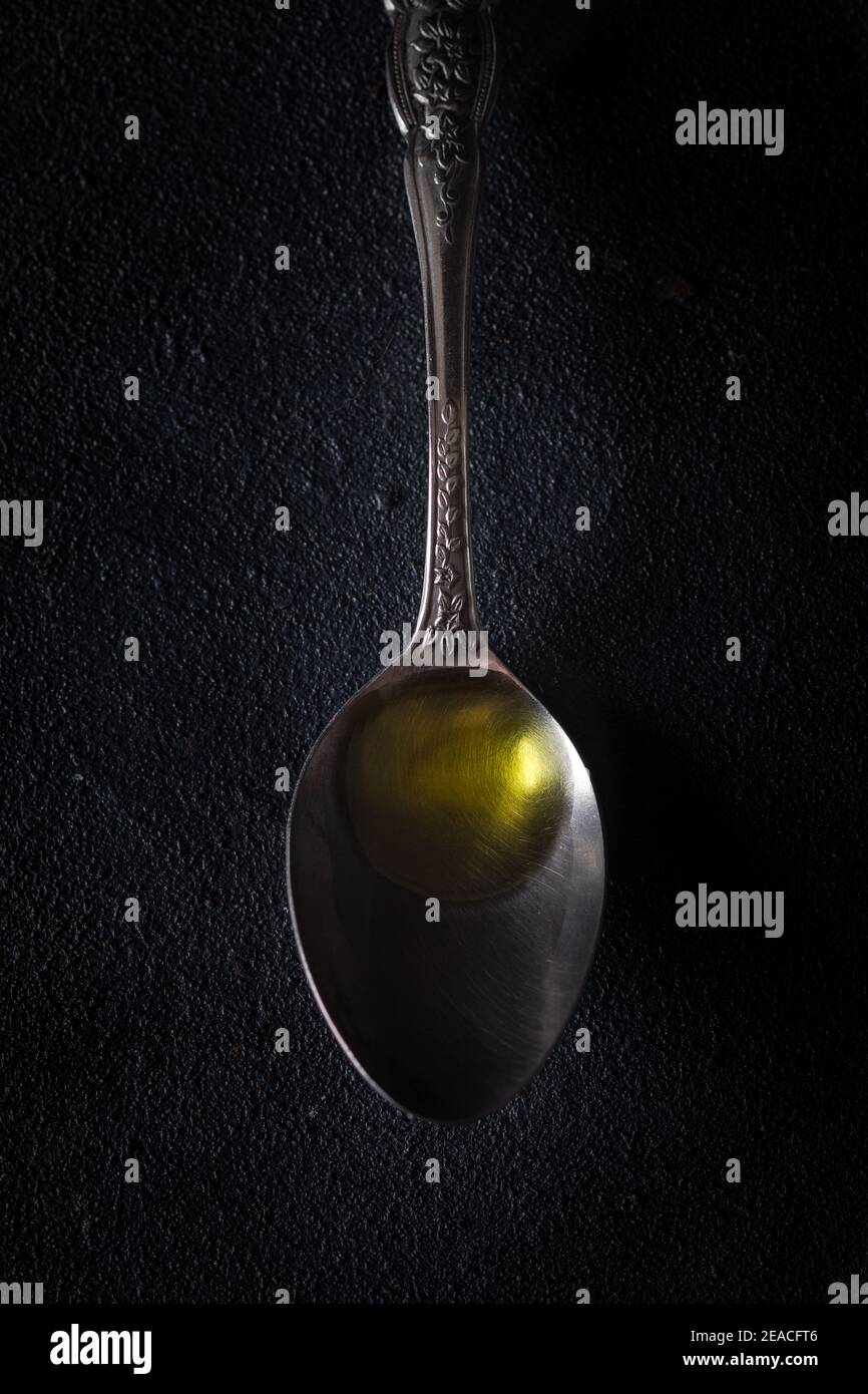 Cucchiaio di metallo con olio d'oliva vergine su fondo scuro. Foto Stock