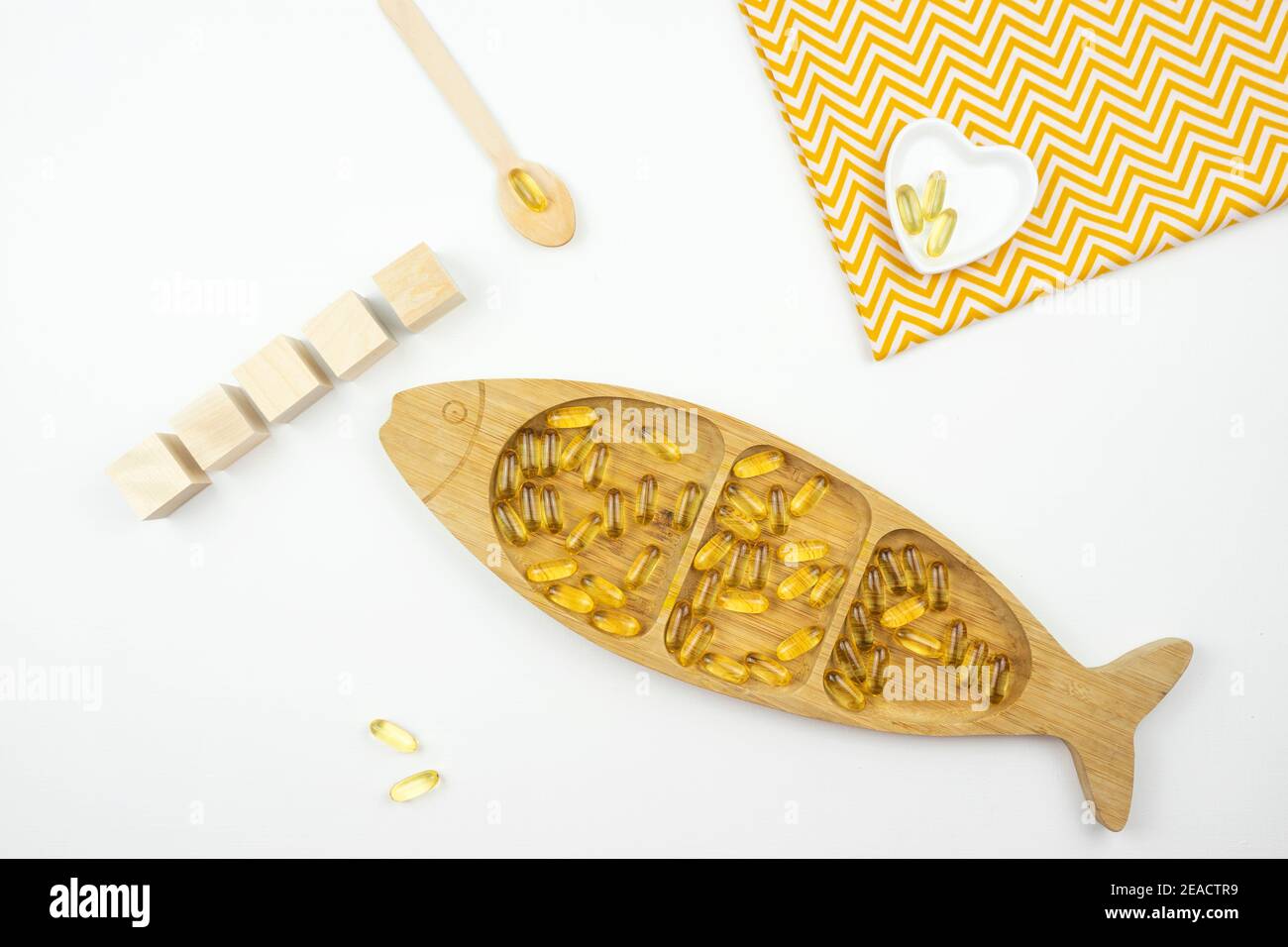 Le capsule gialle di Omega 3 giacciono su una piastra di legno sotto forma di pesce Foto Stock