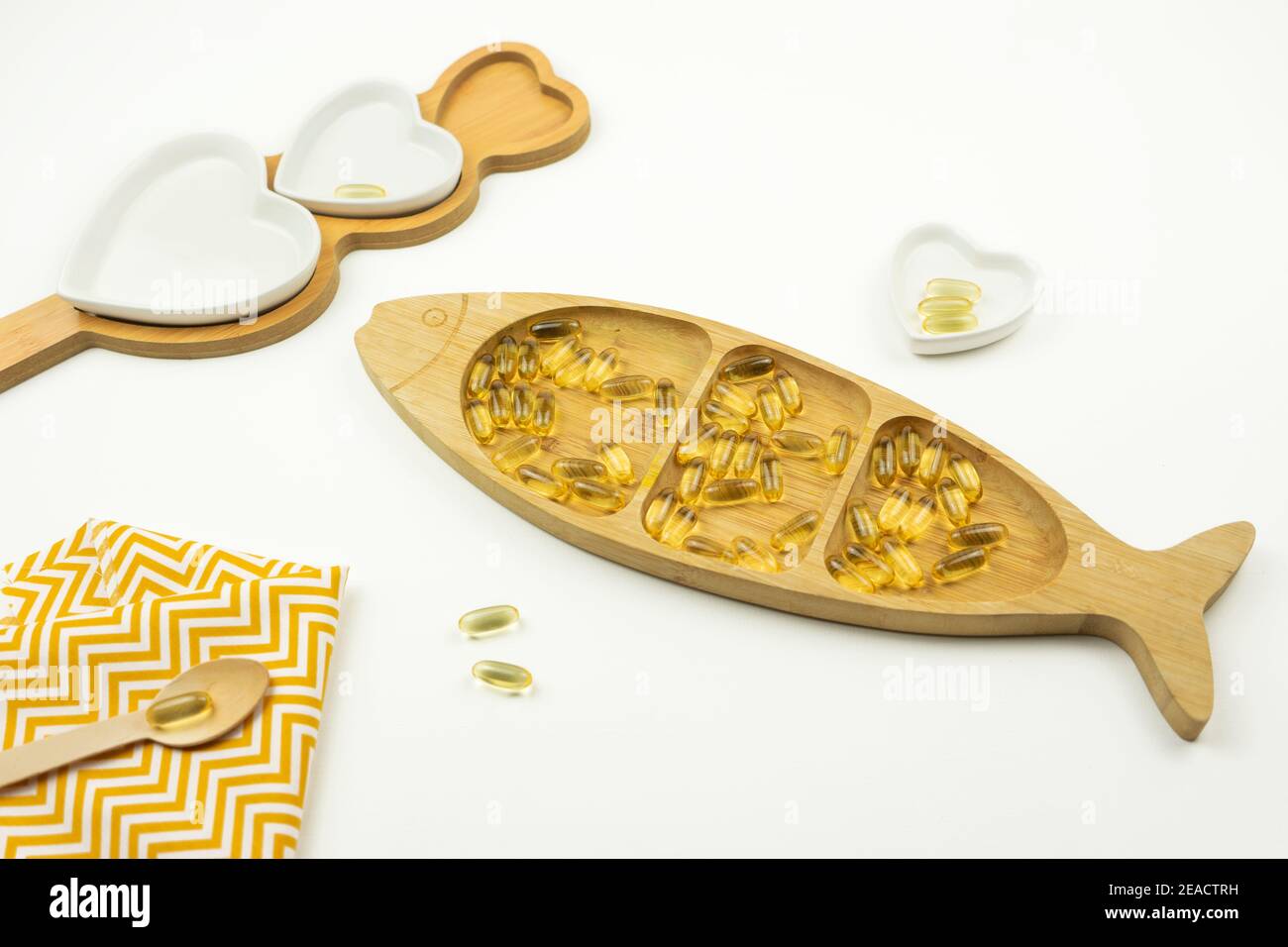 Le capsule gialle di Omega 3 giacciono su una piastra di legno sotto forma di pesce Foto Stock