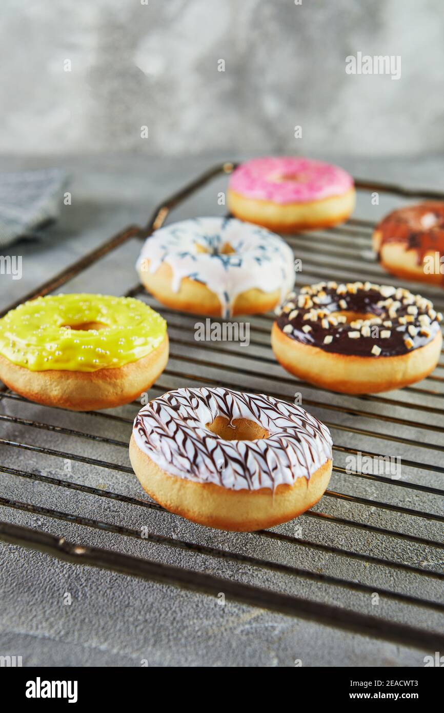 Ciambelle multicolore con smalto e spruzzare su un supporto metallico dal forno e un tovagliolo grigio. Foto Stock