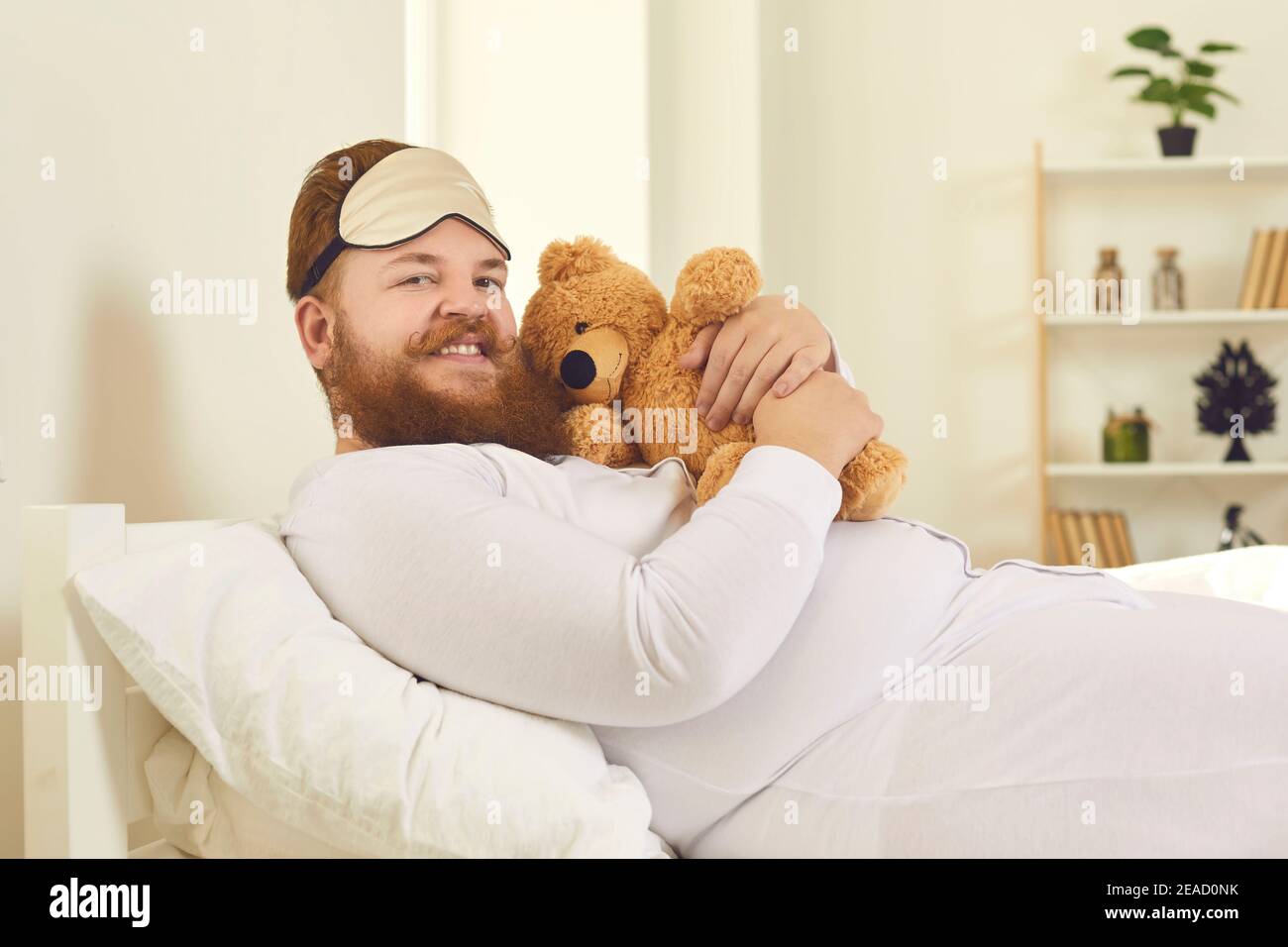 Uomo divertente in pigiama bianca sdraiato con il giocattolo a letto Foto Stock