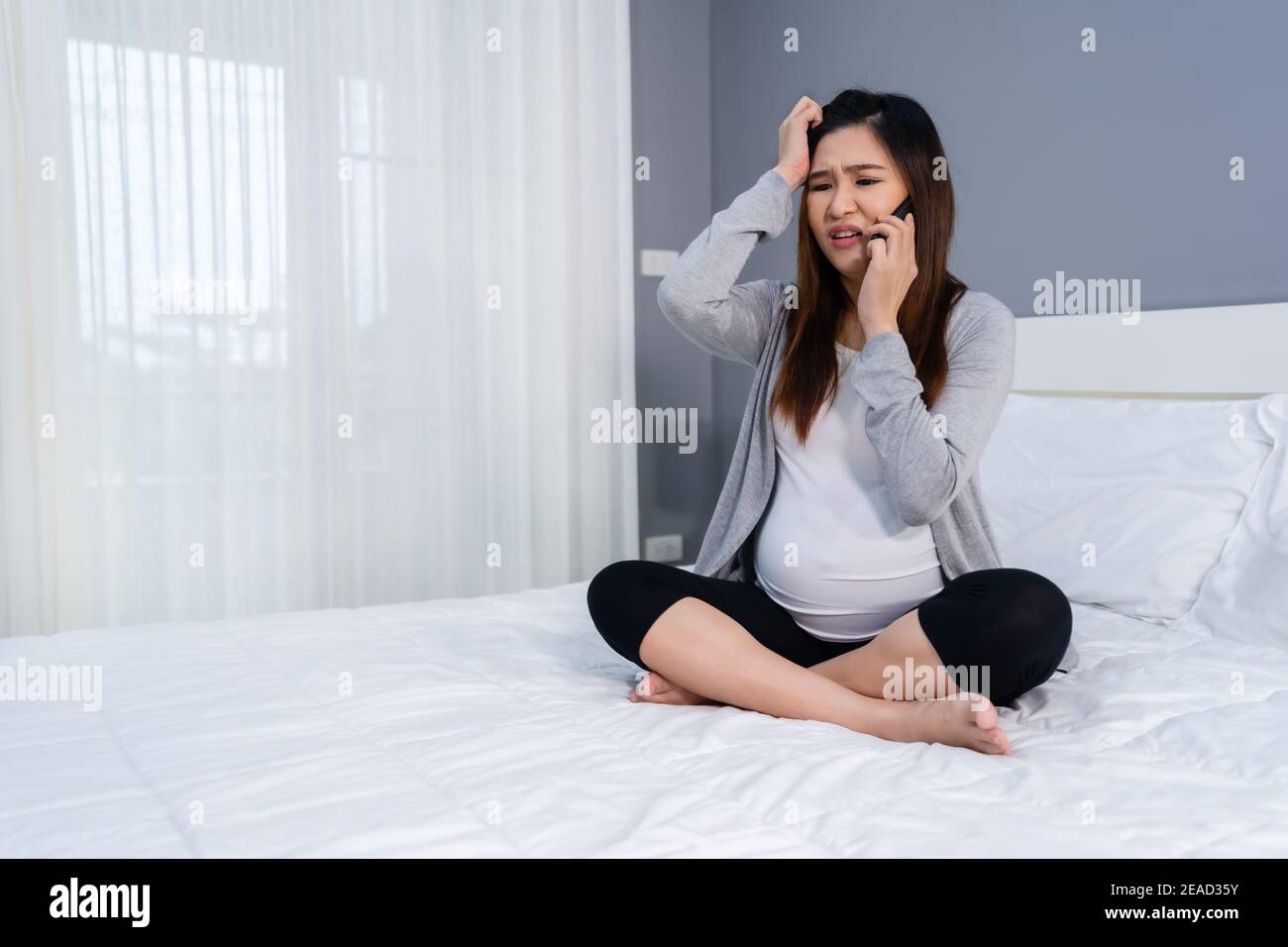 donna incinta stressata che parla su un telefono cellulare in un letto Foto Stock