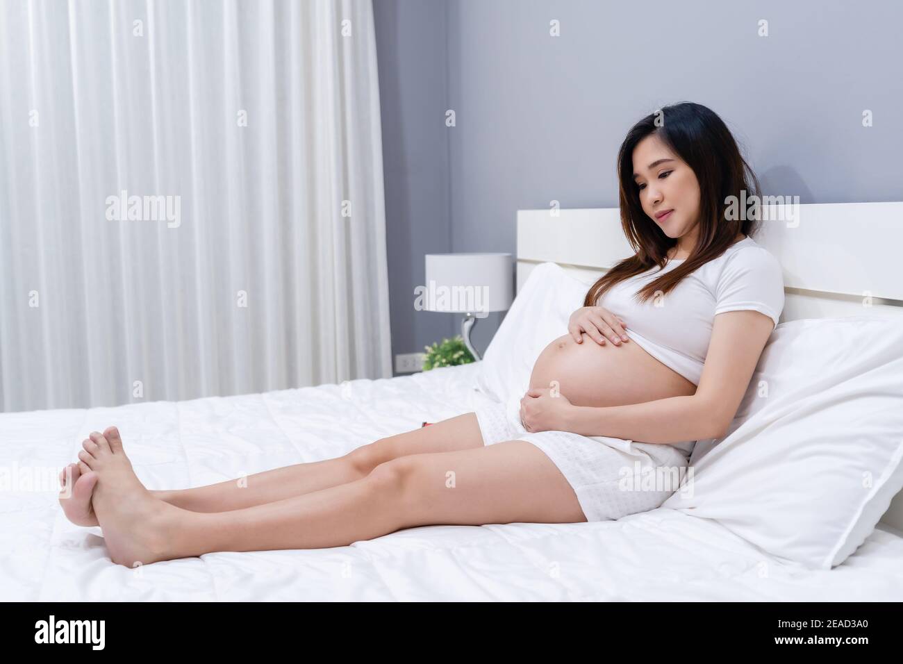 donna incinta che stropica il ventre su un letto Foto Stock
