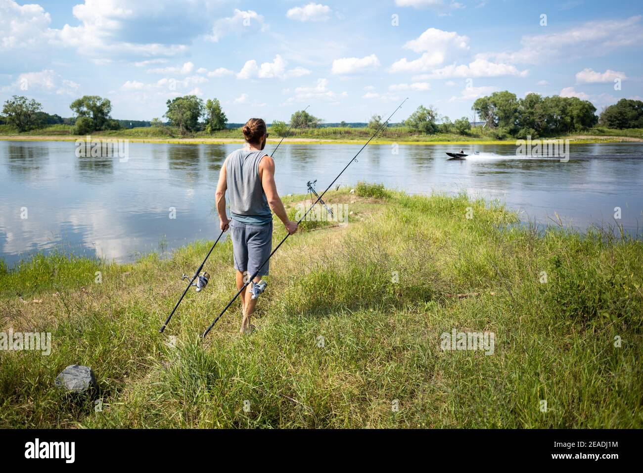 Uomo che porta due canne da pesca carpa verso la riva del fiume Foto Stock
