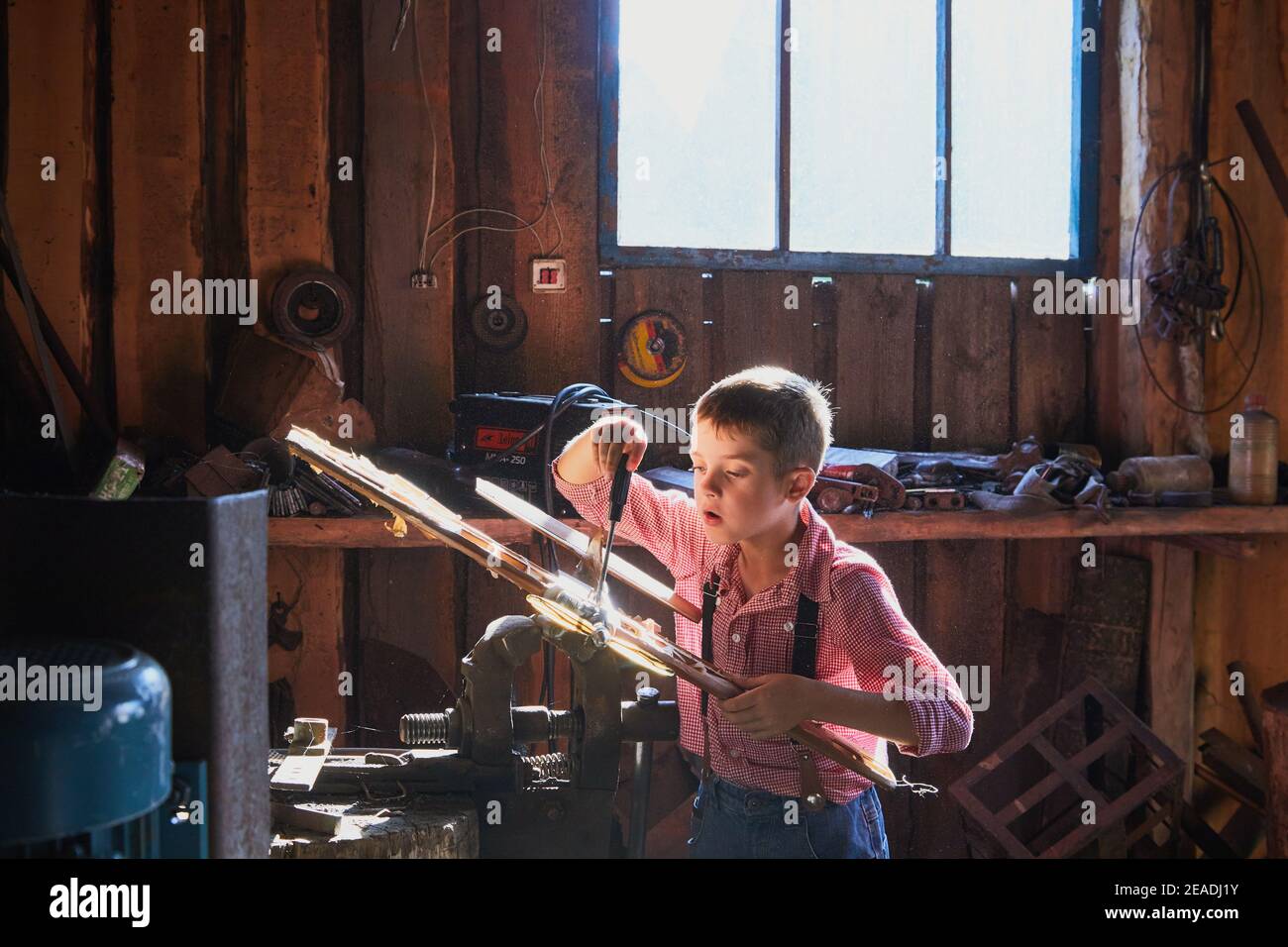 Un ragazzo curioso sta cercando di fissare un vecchio aereo in legno fatto a mano in un laboratorio di Falegnameria. Foto Stock