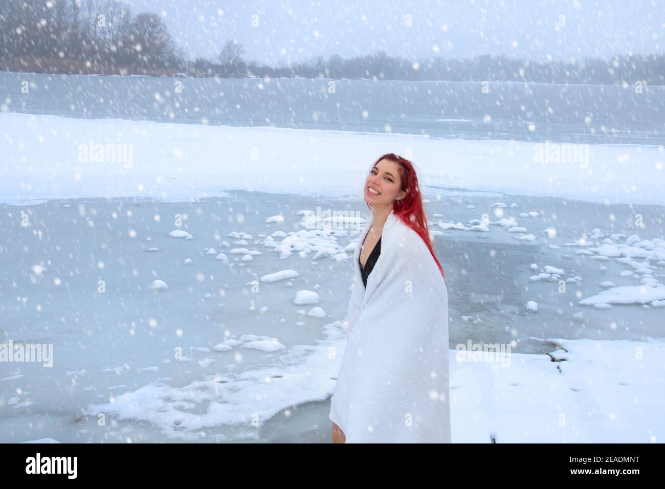 Donna rossa avvolta in un asciugamano con un sorriso felice godendo la terapia fredda sul lago di congelamento, indurente sulla neve, bagno di ghiaccio, e concetto di nuoto invernale Foto Stock