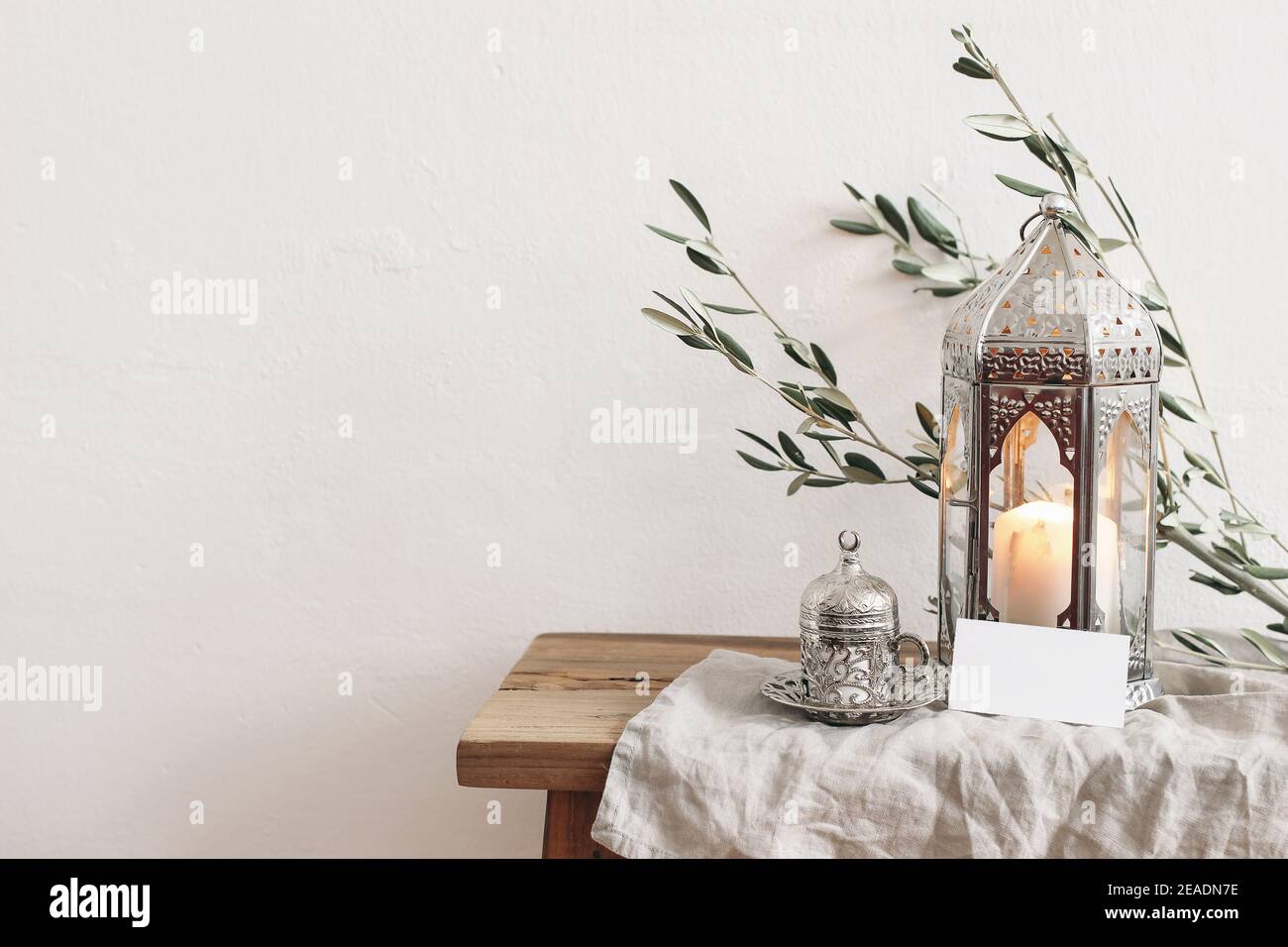 Ramadan Kareem biglietto d'auguri, invito mockup. Lanterna d'argento con candela bruciante e coppa d'argento con tè o caffè. Rami di ulivo verde su Foto Stock