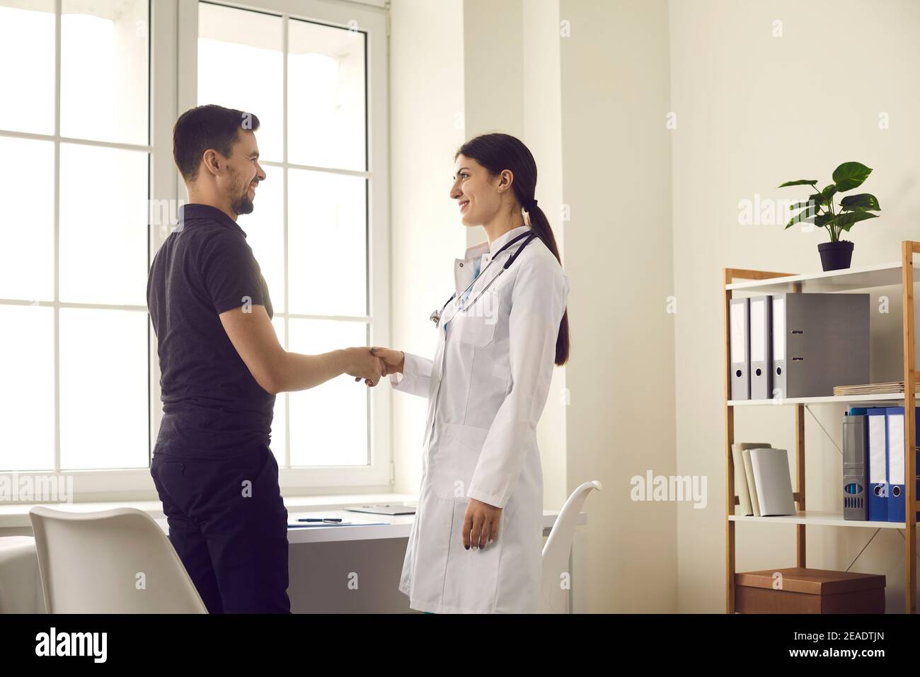 Felice giovane medico e paziente sorridente e scuotendo le mani prima colloquio medico Foto Stock