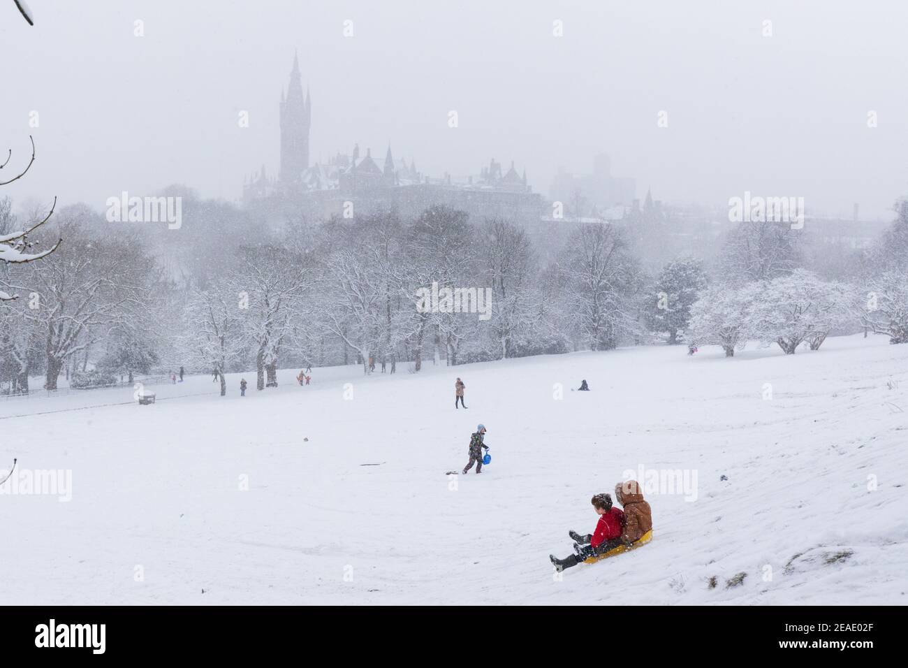 Le persone che si godono la neve invernale a Kelvingrove Park Glasgow UK. Bambini su slitta. Sciare nel parco. Ciclista. Tempesta invernale. Università di Glasgow. Foto Stock
