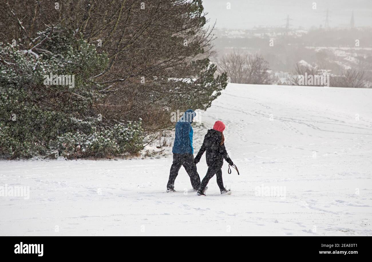 Holyrood Park Edimburgo, Scozia, Regno Unito. 9 febbraio 2021. Il Parco Holyrood innevato ha incoraggiato le persone a giocare e ad allenarsi tra le docce. Coppia che cammina in una doccia di neve pesante. Foto Stock