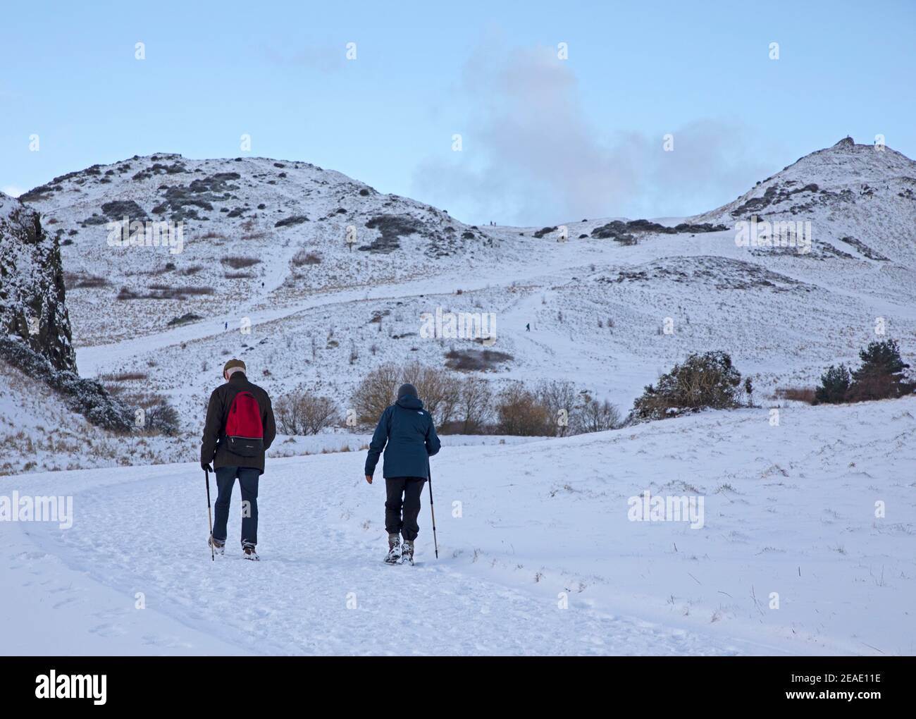Holyrood Park Edimburgo, Scozia, Regno Unito. 9 febbraio 2021. Il Parco Holyrood innevato ha incoraggiato le persone a giocare e ad allenarsi tra le docce. La coppia più anziana usa il palo per camminare nella strada coperta di neve con Arthurs Seat sullo sfondo. Foto Stock