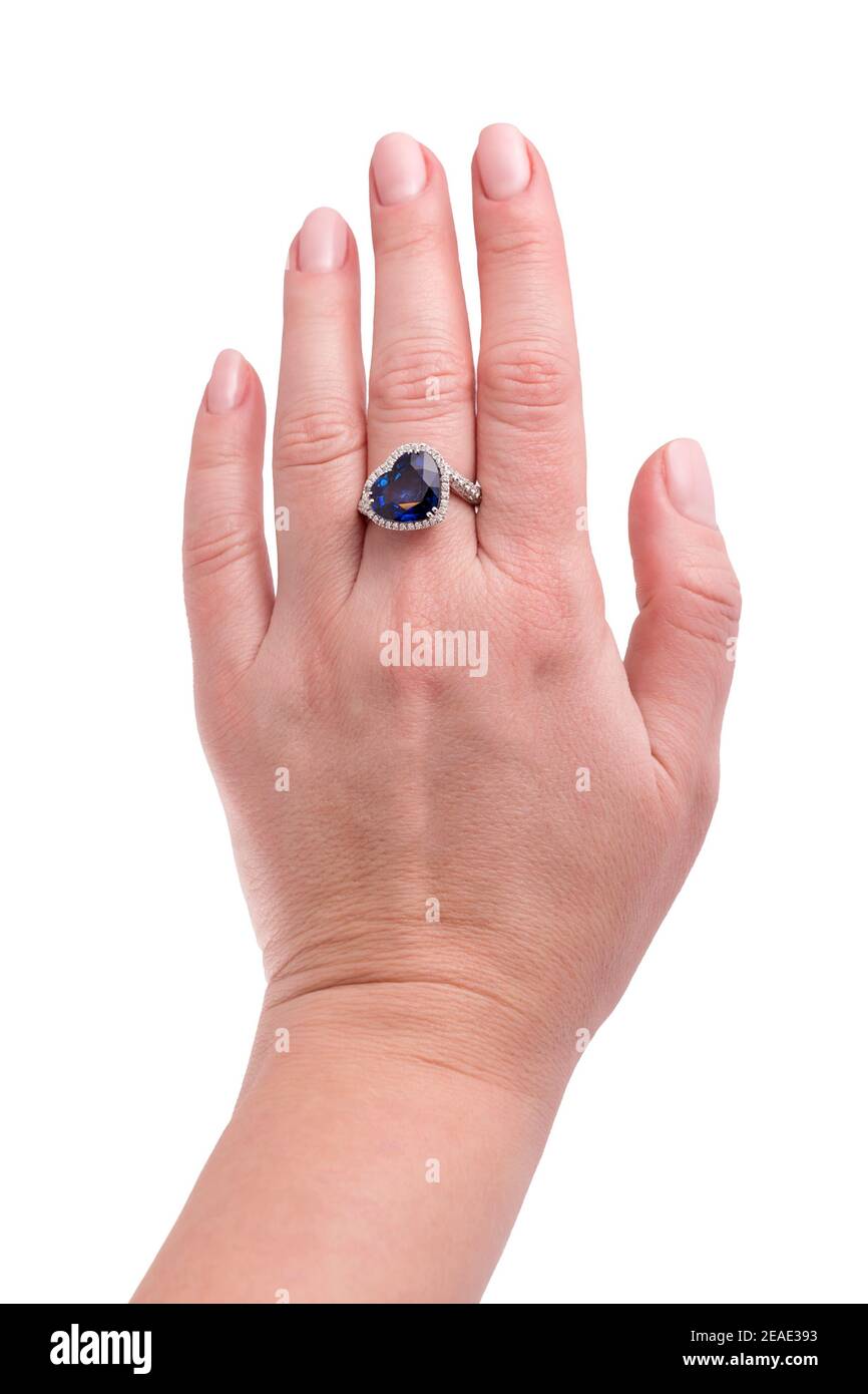 Zaffiro blu a forma di cuore anello prezioso su mano donna isolato su sfondo bianco. Primo piano dell'anello diamantato sulla mano femmina. Anello dorato bianco con Foto Stock