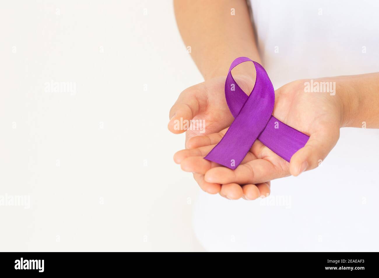 Mani che tengono il nastro viola o viola su tessuto bianco con spazio per la copia. Cancro pancreatico, consapevolezza del cancro testicolare, sopravvivenza del cancro, Leiomiosarcoma Foto Stock
