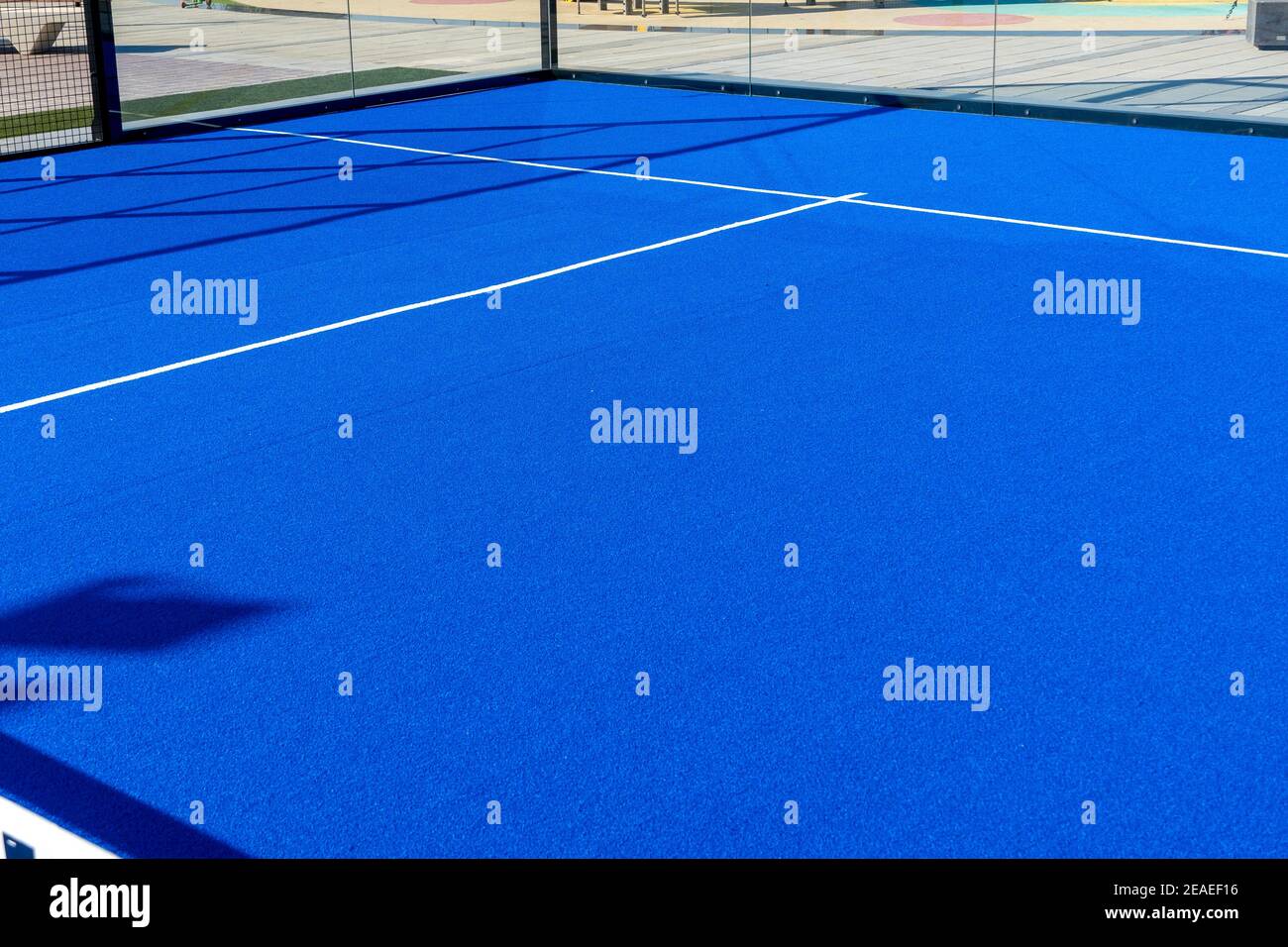 Vista dal campo da tennis, da paddle ball o da pickleball di colore blu brillante, dalla rete alle cabine di servizio e alla linea di base all'aperto. Foto Stock