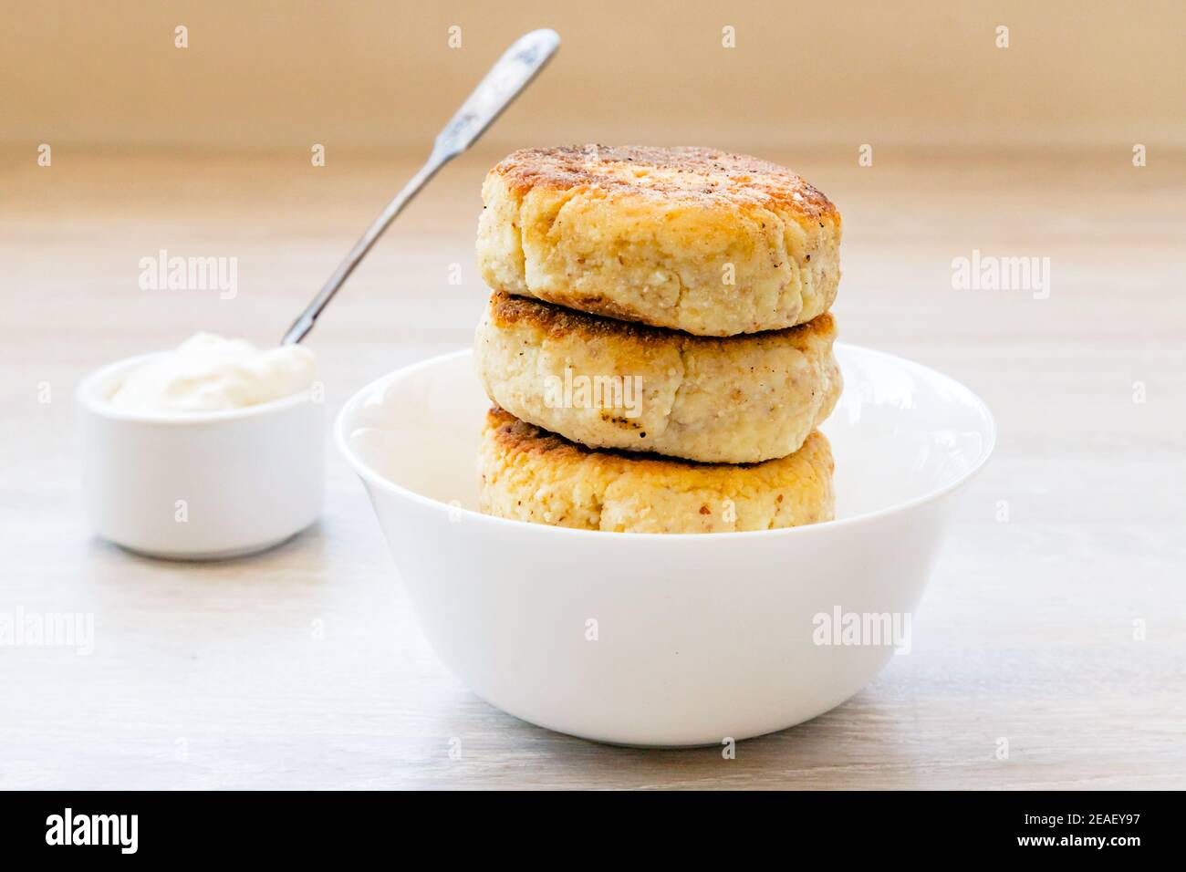 Frittelle dolci caserecce scirniki in ciotola bianca, padella di salsa, panna acida, cucchiaio sul tavolo Foto Stock