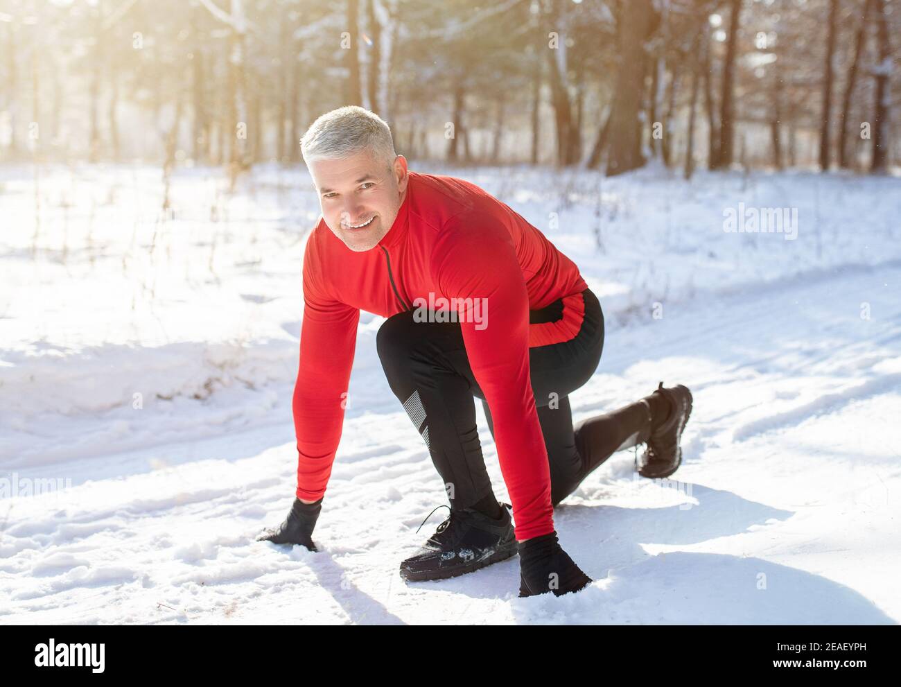 Uomo anziano pronto a correre durante l'allenamento invernale all'aperto in condizioni di neve fredda. Allenamento stagionale e stile di vita attivo Foto Stock