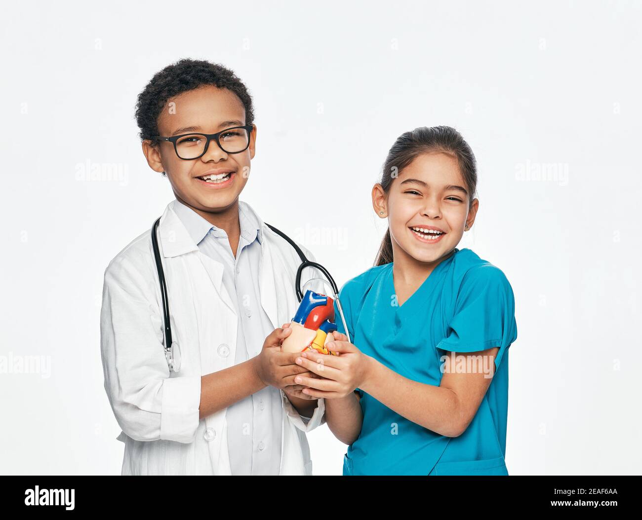 Due bambini positivi che indossano un'uniforme medica stanno tenendo un modello anatomico del cuore. Concetto di cura cardiaca Foto Stock