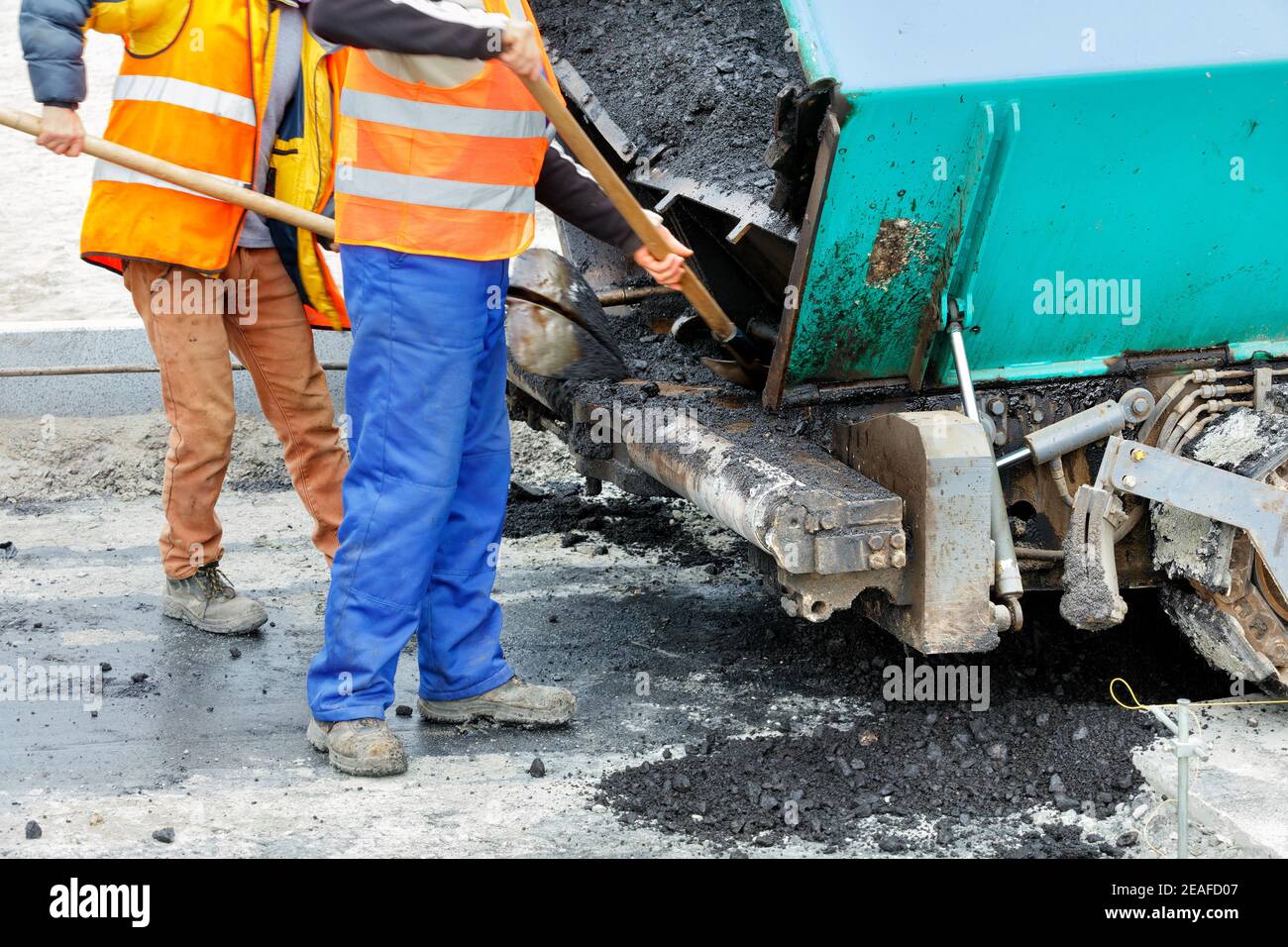 I lavoratori utilizzano pale per pulire un'asfaltatrice davanti agli elementi di costruzione di una nuova sezione della strada. Messa a fuoco selettiva. Foto Stock