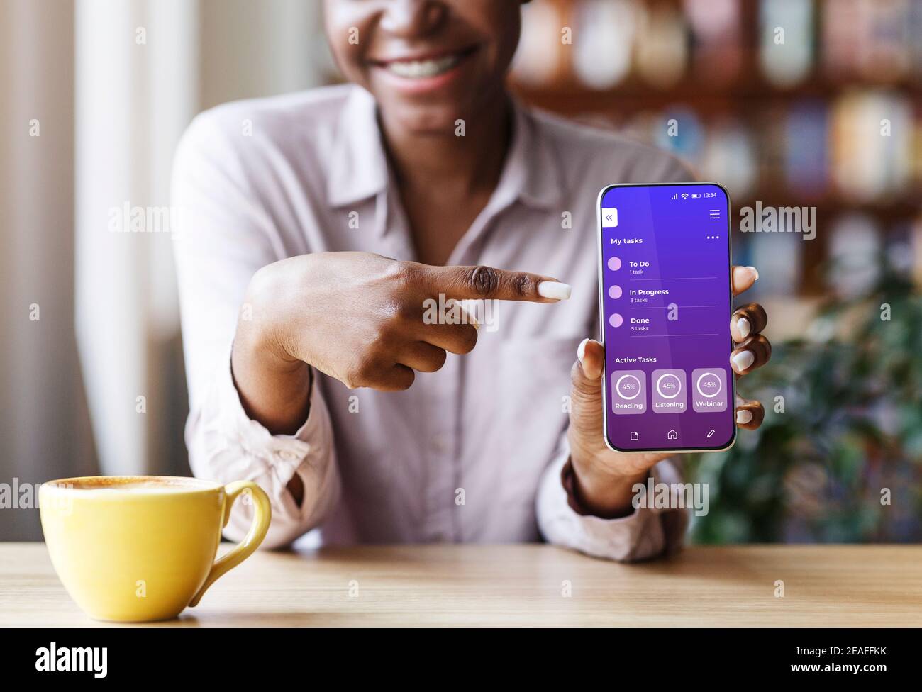 Donna nera irriconoscibile che mostra l'app didattica aperta sullo smartphone, puntando sullo schermo Foto Stock